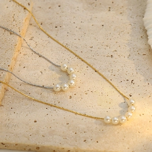 Elegant 18k gold and silver titanium necklaces with pearls on a textured stone surface