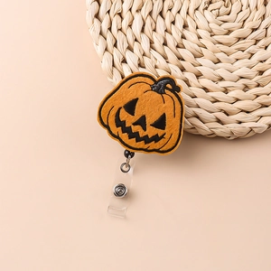 Close-up of Halloween orange pumpkin badge reel with retractable clip on beige background