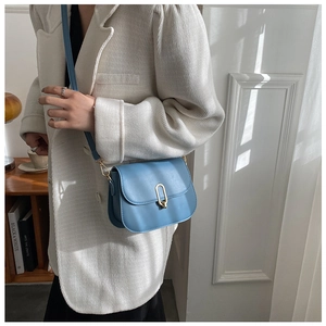 Detail of light blue saddle bag with gold metal clasp on beige pleated blazer