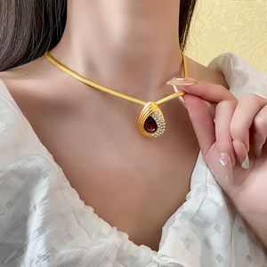 Close-up of gold snake chain necklace with a ruby-red water drop pendant and small diamonds