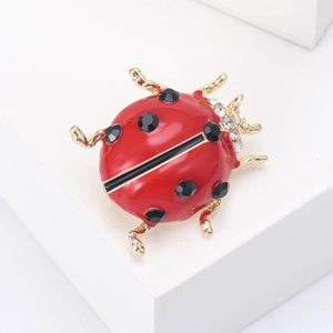 Detailed close-up of a red ladybug brooch with gold trim and black rhinestones on white