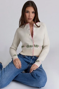 Detail of cream knit cardigan with pink scalloped trim and embroidered floral bow pattern