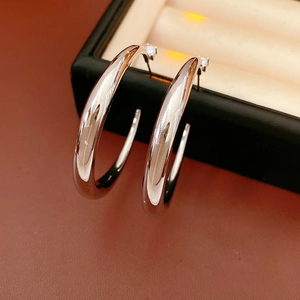 Close-up of silver C-shaped hoop earrings with zircon studs on a black display stand