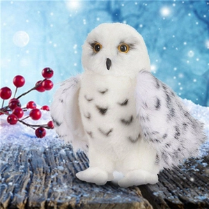 Close-up of a white snowy owl plush toy with grey spots perched on a wooden branch