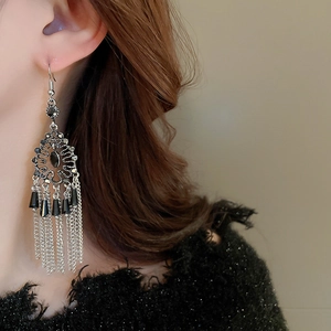 Close-up of long silver tassel earrings with black rhinestones on a female model