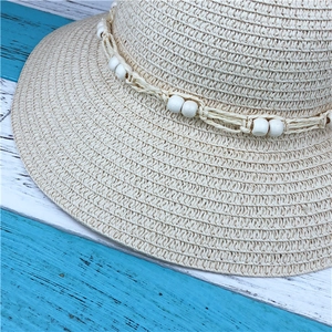 Close-up of beige woven sun hat texture featuring decorative white bead strap detail