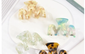 Close-up of acetic acid wave hair claws in marbled amber, beige, and emerald tones