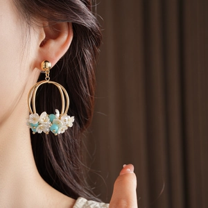 Close-up of golden floral earrings with teal beads and white flowers on model