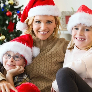 A happy family wearing plush red Christmas hats in front of a festive tree