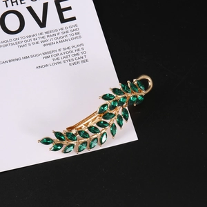 Detailed close-up of leaf-shaped gold hair clip with green marquise crystals