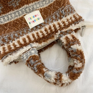 Close-up of the striped sherpa fleece texture and metal zipper of the plush tote bag