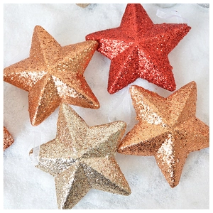 Close-up of sparkling red and gold glitter star ornaments on a white snowy background