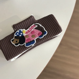 Detailed embroidery of a cartoon dachshund with Happy text on brown ribbed fabric
