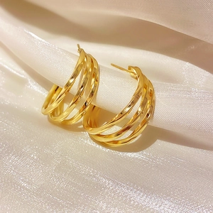 Macro shot of gold layered hoop earrings on white silk fabric with mirror finish shine
