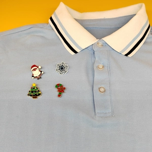 Detailed view of four Christmas enamel pins including Santa and tree on a blue polo shirt