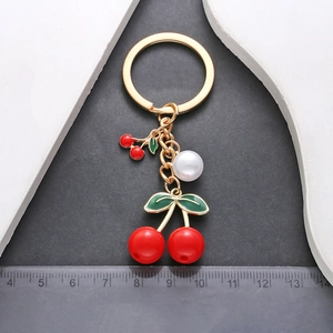 Red cherry pearl keychain with gold alloy ring and green leaf charms on dark background