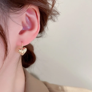 Close-up of a gold pleated heart earring worn by a model to show texture and size