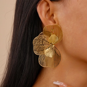 Close-up of model wearing large hollow metal flower earrings with golden layered petals
