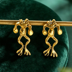 Macro detail of vintage golden frog stud earrings displayed on dark green velvet background