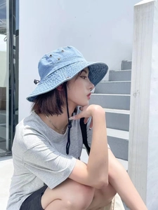 Détail d'un bob en jean bleu clair avec œillets métalliques et cordon coupe-vent réglable