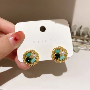 Detail of gold twisted earring with green crystals and pearls held by hand