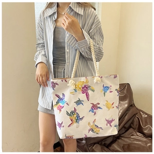 Linen-look tote bag with colorful turtle prints and rustic rope handles shown with model
