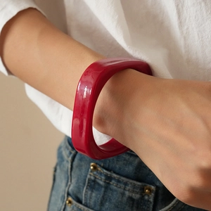 Close-up of a wide red resin geometric bangle with glossy finish on a female model