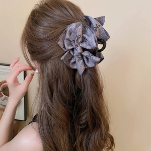 Macro shot of a taupe fabric bow hair claw with elegant black ribbon print on long hair
