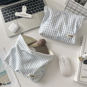Trousse à maquillage bleue à carreaux brodée de fleurs près d'un ordinateur