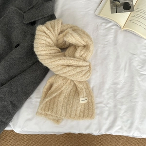 Detail of beige knit wool scarf with LOVELORN label on a stylish bed setting