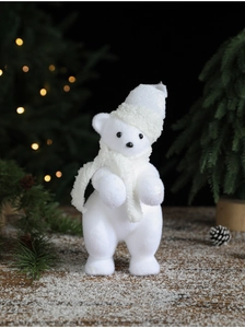 Close-up of white flocked Christmas bear ornament on snowy wood with bokeh lights