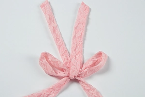 Close-up of light pink floral lace fabric with intricate cutouts and a delicate bow detail