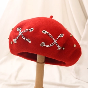 Red wool beret hat with punk silver metal chain and rhinestone studs on beige background