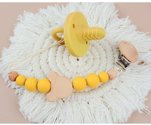 Detail of yellow silicone pacifier and wooden bear clip on a white woven mat