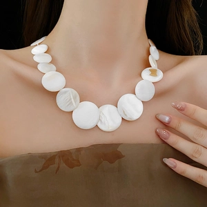 Detail shot of a bohemian geometric white shell necklace worn by a model in soft light