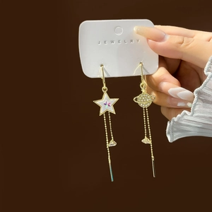 Detail of asymmetric gold tassel earrings with star and planet crystal charms