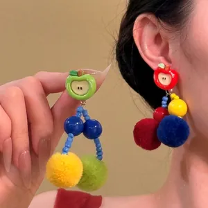 Close-up of asymmetric apple earrings with colorful pom poms on a model's ear