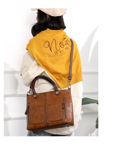 Brown PU leather tote bag with front pockets shown on shoulder in a lifestyle setting