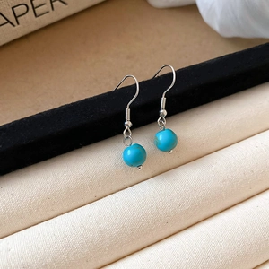 Close-up of silver spring ear hooks with turquoise blue round bead pendants on fabric