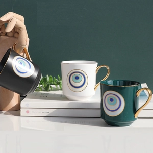 Three ceramic evil eye mugs in black, white, and green with elegant golden handles