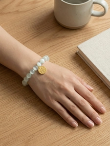 Detail view of cat eye bead bracelet with a golden Fu pendant on the wrist