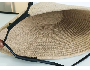 Macro detail of natural straw tote bag featuring spiral weaving and wooden bead accents