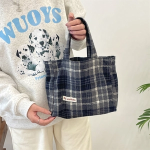 Close-up of blue and white plaid tweed tote bag held by model for casual style