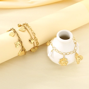 Close-up of golden charm bracelets with heart, bear, and sunflower pendants on satin fabric