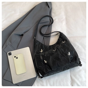 Flat lay of large capacity black pleated tote bag with silver butterfly accent and iPad