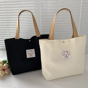 Detail of canvas tote bags in black and beige with a lovable dog patch and sturdy handles