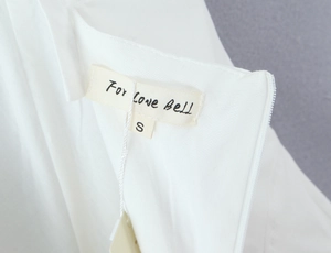 Detalle de vestido blanco con escote cuadrado mostrando tejido y la etiqueta talla S