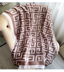 Detail of soft silk-like scarf with geometric pattern draped on a beige chair