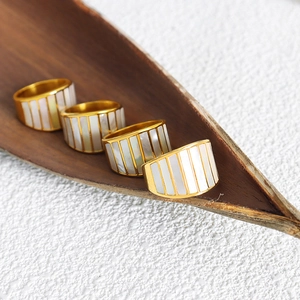 Gold wide band rings with white shell inlay on a brown leaf against white background