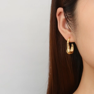 Close-up of golden irregular lava-style C-shaped earrings on a female model's ear